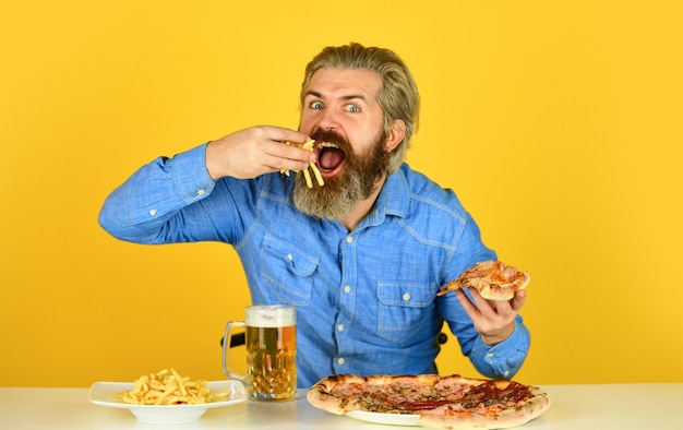 Guy in bar drinking beer glass and eating pizza Cheers watching football on TV american fast food happy bearded man with beer and pizza italian food French fries