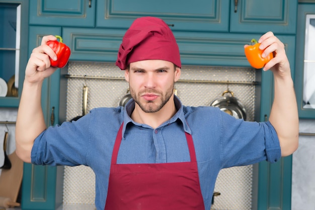 Photo guy chef in hat, apron hold at pepper vegetable in kitchen. vegetarian, health, diet concept. food, cooking, culinary, cuisine.