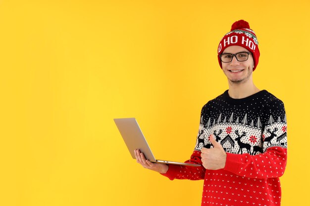 Guy in Christmas sweater with laptop on yellow background