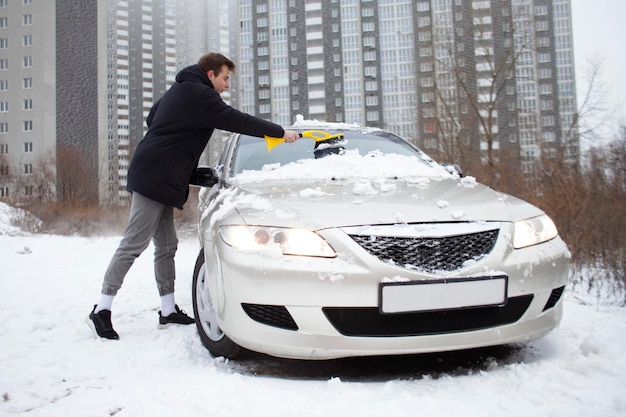 Guy cleans the snow with a brush from the car a man takes care of the car in winter