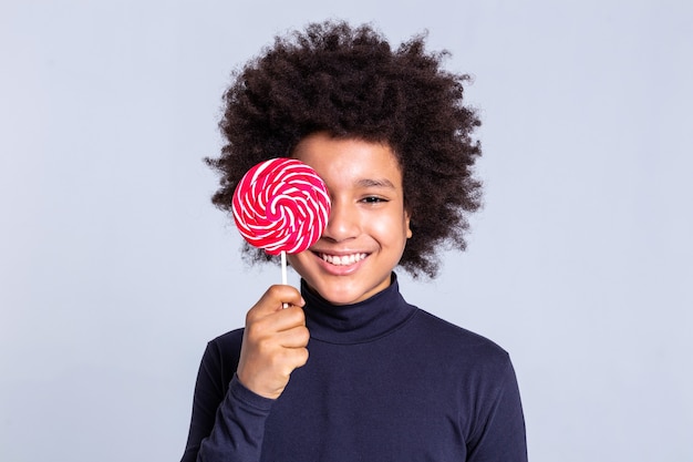 Guy closing face. Cheerful African American kid with wild hair covering face with big candy and showing his wide smile