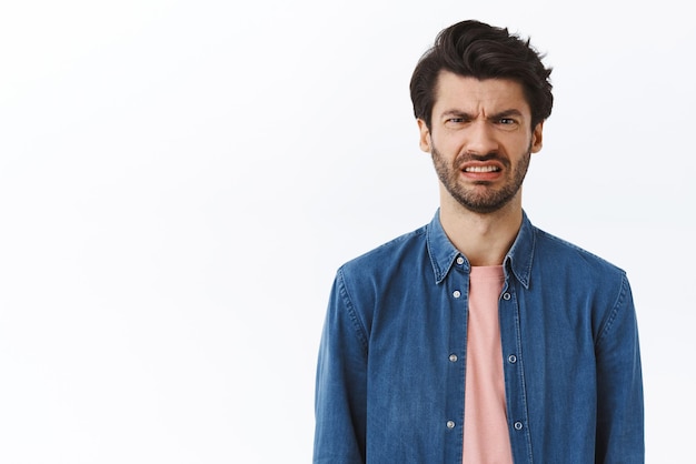 Guy cringe as looking at awful disgusting scene Displeased bothered handsome man frowning feeling sick express aversion grimacing reluctant disappointed standing over white background