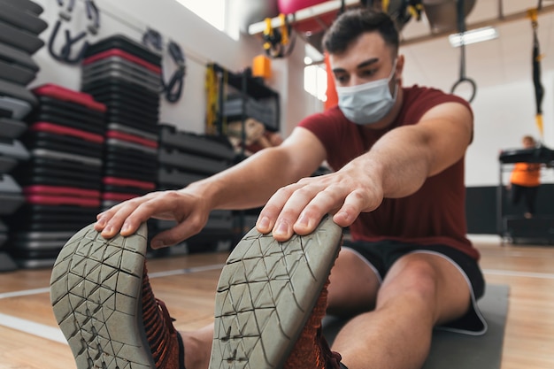 Guy does stretching in the gym with mask