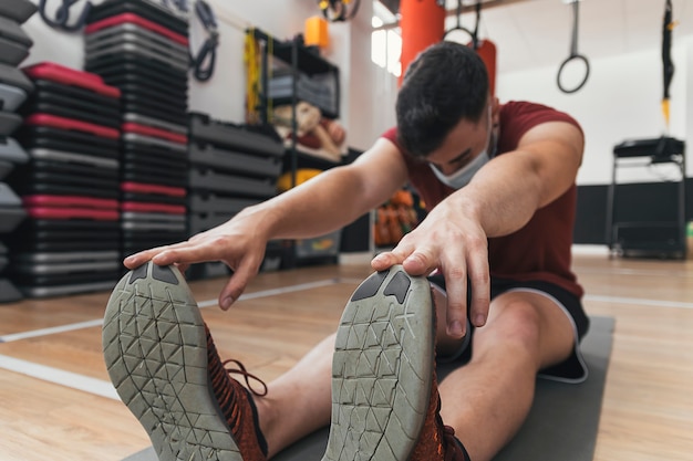 Guy does stretching in the gym with mask