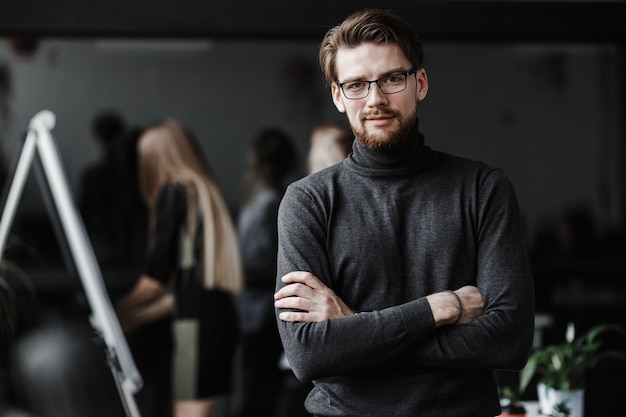 The guy dressed in casual office style clothes and glasses stands in the modern office