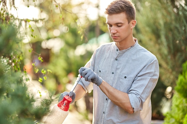 Guy gardener sprays water on plants in the beautiful nursery-garden on a sunny day. Work in the gardener .