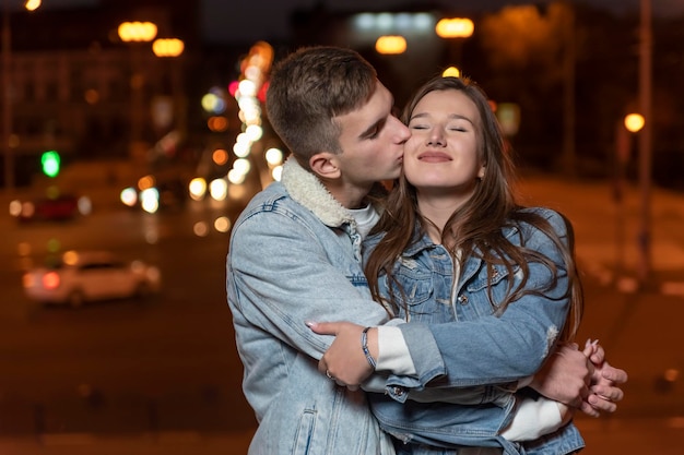 Guy gently hugs and kisses his girlfriend on evening city background