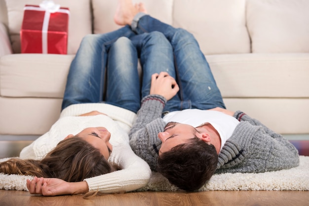 The guy and girl are lying on floor with their legs on sofa.