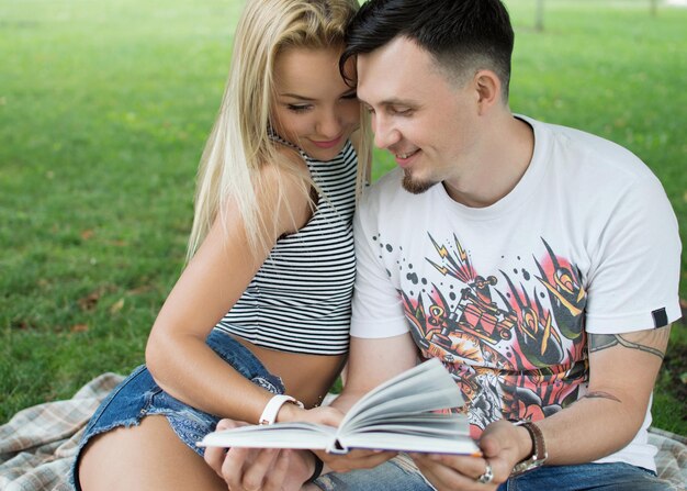 A guy and a girl are reading a book in a city park on a hot summer day Students relax on a green lawn and read a book