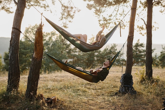 A guy and a girl are relaxing in hammocks in a pine forest at sunset