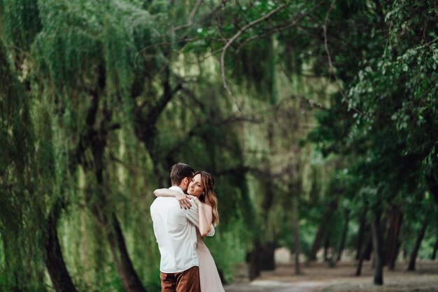 A guy and a girl are walking along the banks of a wild river overgrown with willows and forest