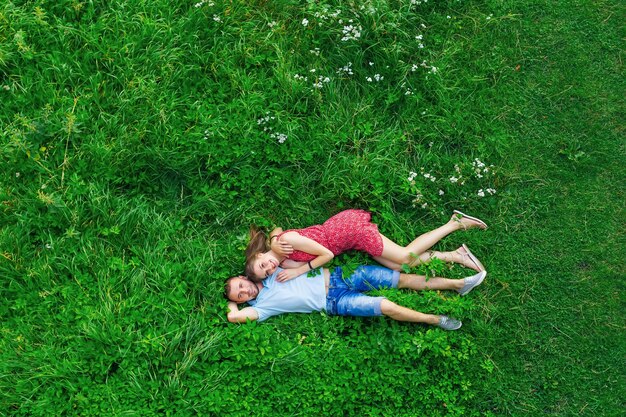 Photo guy and girl hugging each other on green grass and look at camera. top view.