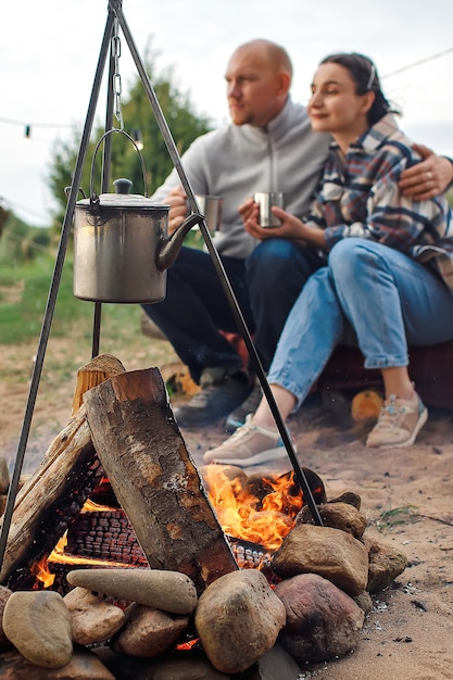 A guy and a girl with mugs in their hands are warming themselves by the fire.