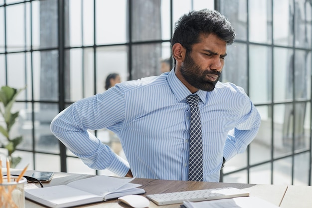 Guy Having Backache Massaging Aching Lower Back Suffering From Pain Sitting At Workplace In Modern Office