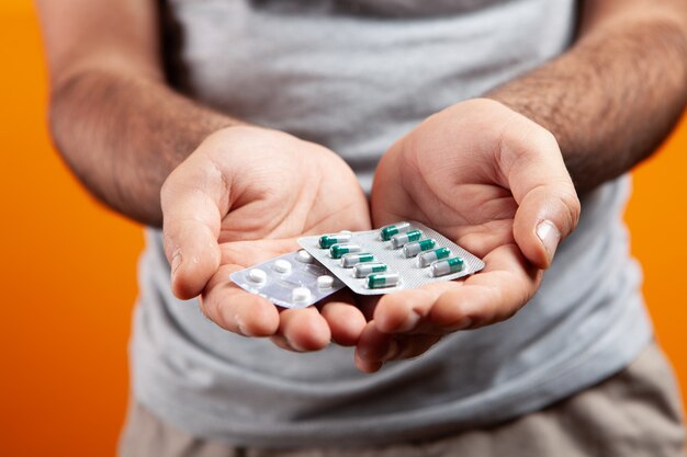 The guy holds capsules and pills in his hands on an orange background