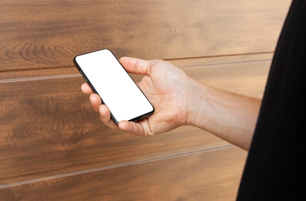 Guy holds mobile phone with blank screen near brown wall