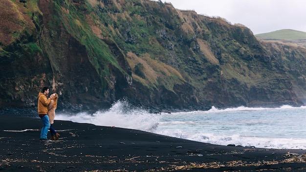 The guy hugs a girl on the background of rocks and the ocean