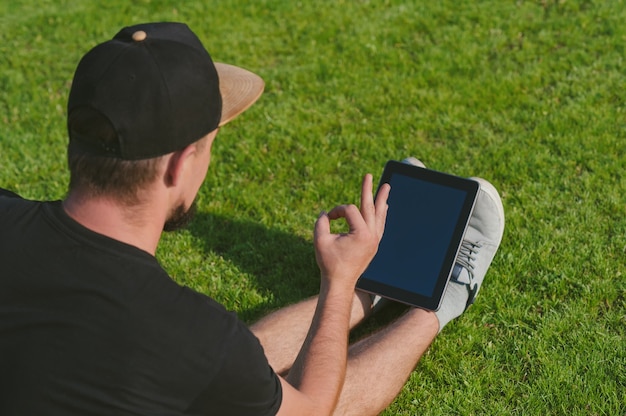 The guy is engaged in online training, on a green lawn with a tablet.