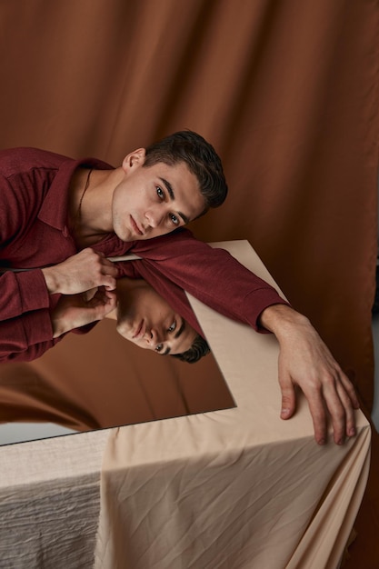 The guy is leaning against the glass at the table indoors and the fabric background