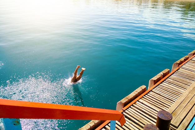 Guy jumps into the water from the pier. Summer vacation