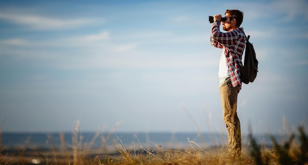 Guy looking at binoculars in hill man in tshirt with backpack