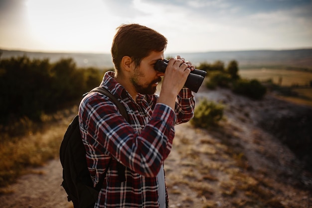 Guy looking at binoculars in hill man in tshirt with backpack