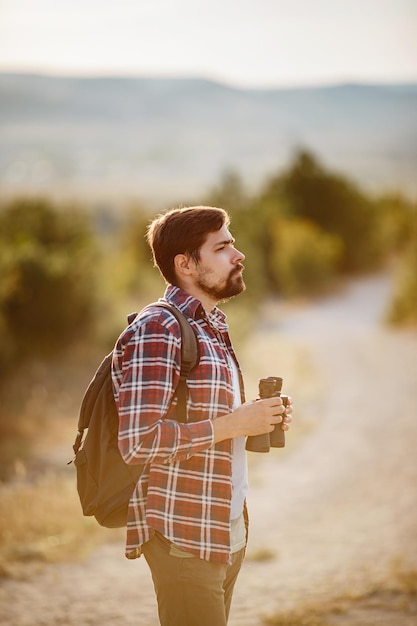 Guy looking at binoculars in hill man in tshirt with backpack