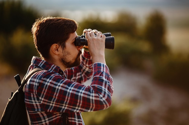 Guy looking at binoculars in hill man in tshirt with backpack