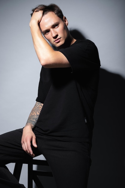 A guy of model appearance in black clothes poses on a gray studio background