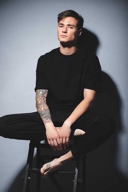 A guy of model appearance in black clothes poses on a gray studio background