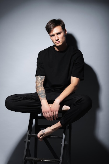 A guy of model appearance in black clothes poses on a gray studio background