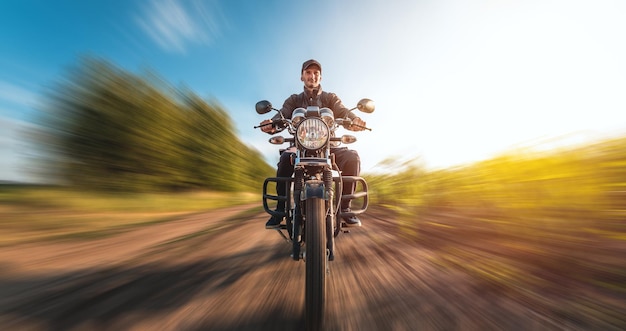 A guy on a motorcycle rides at speed along a dirt road on a sunny day Budget motorcycle moves with a blur effect