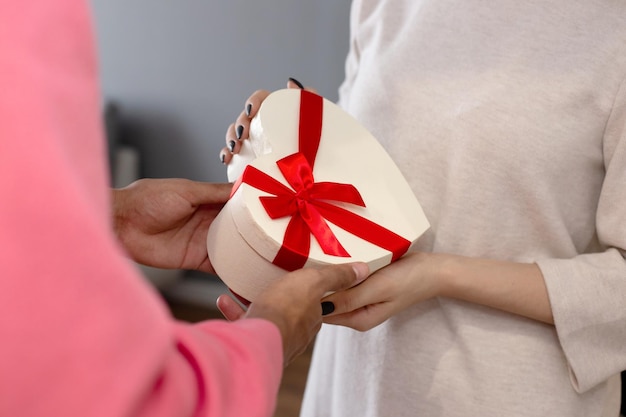 A guy in a pink jumper gives a girl in a white dress a white box in the shape of a heart