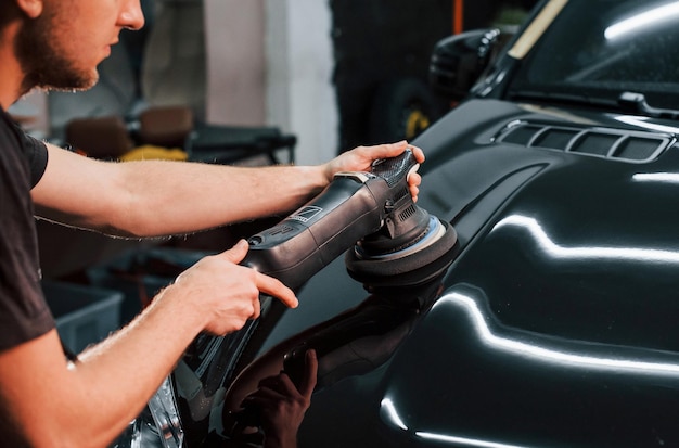 Guy polishing surface of vehicle Modern black automobile get cleaned by man inside of car wash station