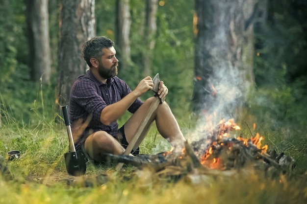 Guy relax at bonfire in forest.