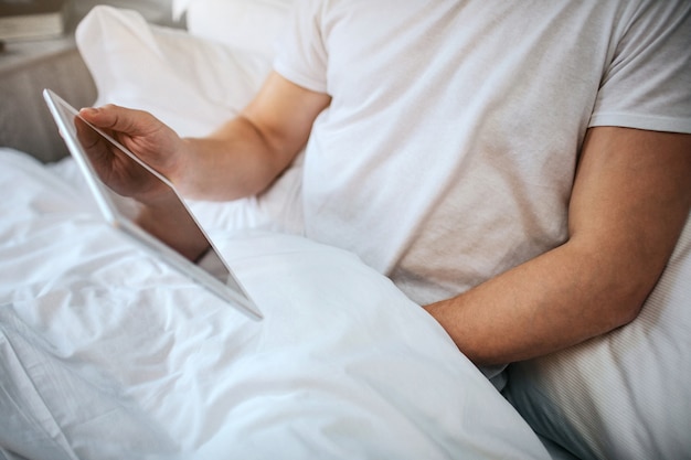 Guy sit in bed in the morning. He hold hand under blanket and masturbating. Man has white tablet in hand