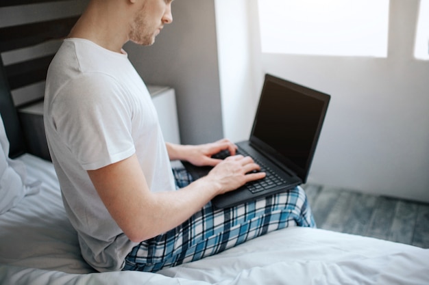 Guy sit at edge of bed and type on keyboard laptop