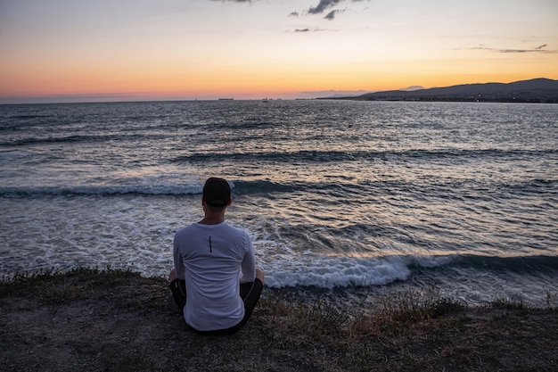 guy sits on the edge of a cliff and looks at the beautiful seascape and waves. Rest and meditation after a long workout.