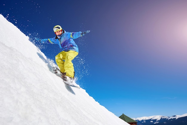 Guy snowboarding down the mountain slope against blue sky