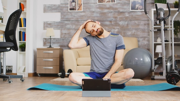 Guy stretching neck muscle watching online fitness lesson on tablet computer.