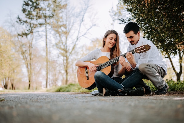 Guy teaching girl how to play guitar at the park.