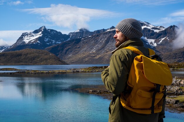 Guy travels with a yellow backpack through picturesque places with beautiful mountain landscapes.