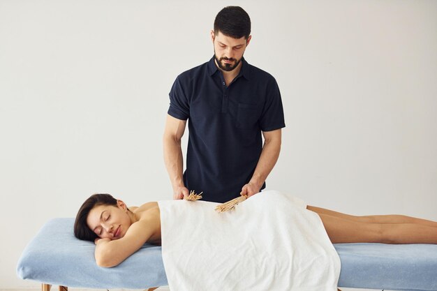 Guy uses special sticks Young woman is lying down when man doing massage of her body at spa