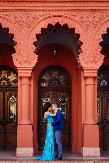 The guy wants to kiss a girl standing under the arch of beautiful red building