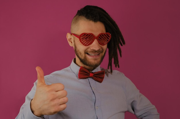 Guy wears heartshaped glasses and bow tie He shows thumbsup gesture with hand