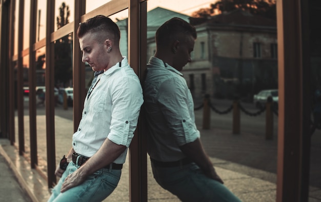 A guy in a white shirt and blue jeans stands with his back on the mirror wall