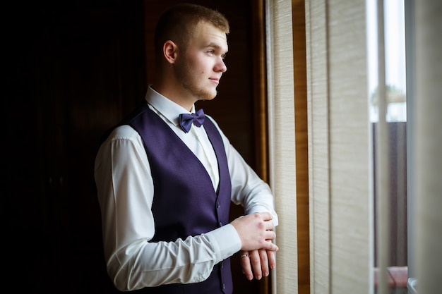 A guy in a white shirt and trousers dresses on a wedding day.