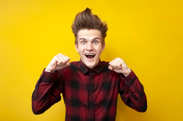 Guy winner with a funny hairstyle screams yes on a yellow isolated background