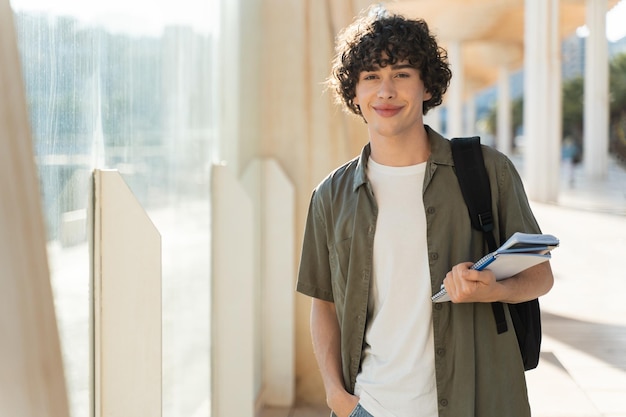 Guy with curly hair holding books and looking at the camera with while walking at the street