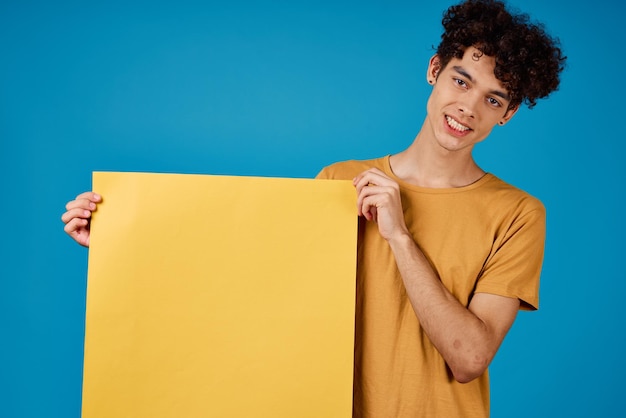 Guy with curly hair of yellow asters in his hands studio blue background